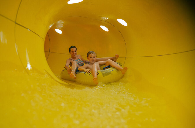 Mutter und Sohn rutschen lachend zusammen eine Wasserrutsche hinunter.
