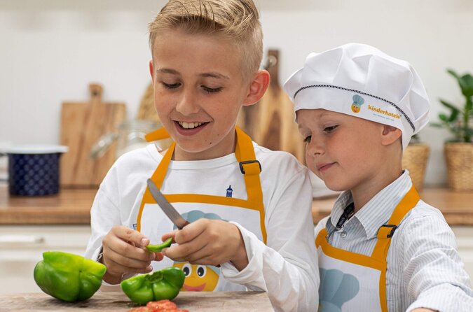 Zwei Jungen mit Schürzen schneiden gemeinsam eine grüne Paprika in der Kinderküche.