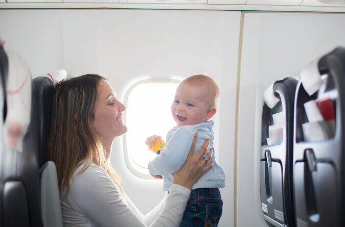 Mutter mit Baby im Flugzeug während einer Reise, beide sitzen am Fenster.