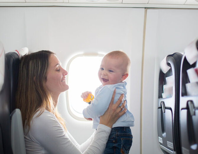Mutter mit Baby im Flugzeug während einer Reise, beide sitzen am Fenster.