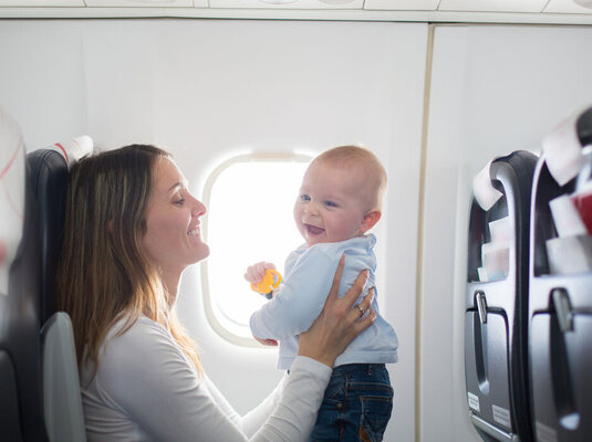 Mutter mit Baby im Flugzeug während einer Reise, beide sitzen am Fenster.