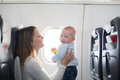 Mutter mit Baby im Flugzeug während einer Reise, beide sitzen am Fenster.