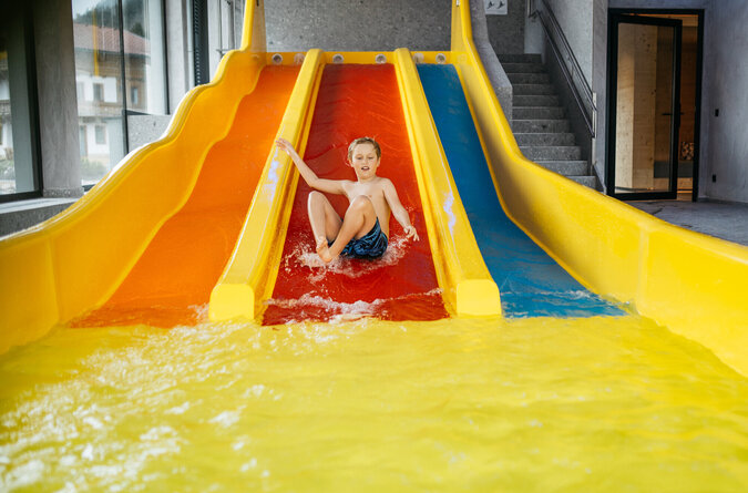 Ein Junge rutscht lachend eine Indoor-Wasserrutsche in einem Kinderhotel hinunter.