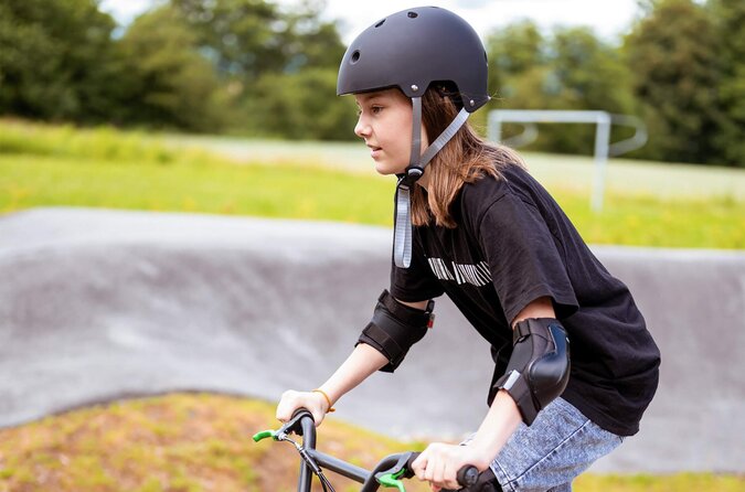 Kind mit Fahrradhelm und Schutzausrüstung fährt fröhlich auf einem Fahrrad im Freien.