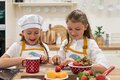 Zwei Mädchen mit Schürzen schneiden Erdbeeren in einer Kinderküche.