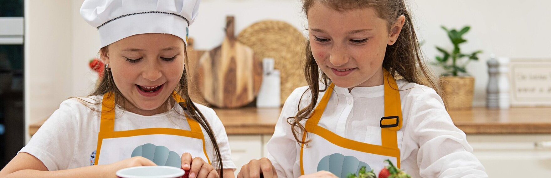Zwei Mädchen mit Schürzen schneiden Erdbeeren in einer Kinderküche.