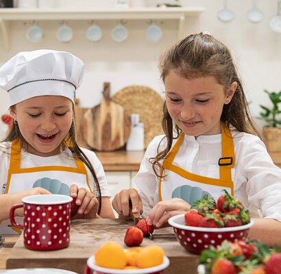 Zwei Mädchen mit Schürzen schneiden Erdbeeren in einer Kinderküche.