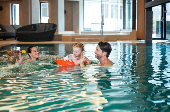 Eine Familie mit Eltern und Kindern spielt lachend zusammen im Pool.
