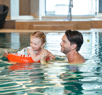 Eine Familie mit Eltern und Kindern spielt lachend zusammen im Pool.