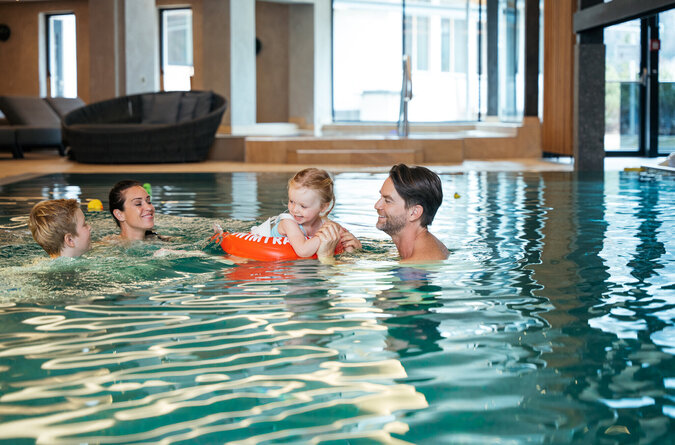 Eine Familie mit Eltern und Kindern spielt lachend zusammen im Pool.