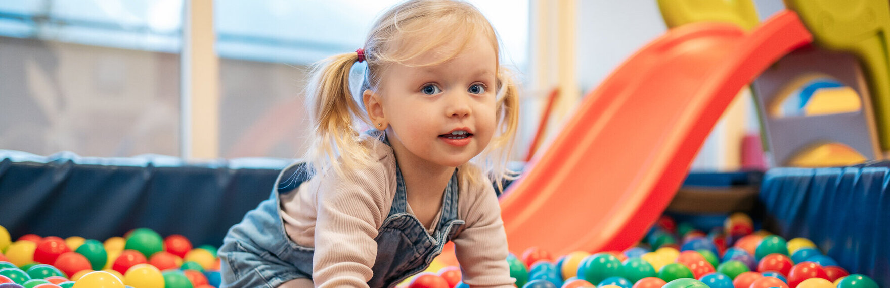 Ein Mädchen spielt im bunten Bällebad eines Kinderhotels.