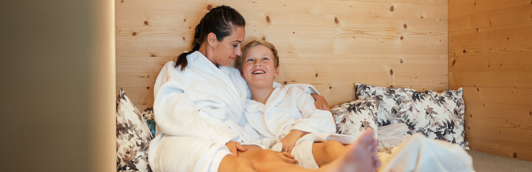 Mutter und Sohn liegen entspannt nebeneinander in Bademänteln.