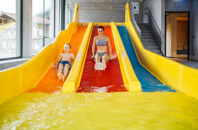 Mutter und Sohn rutschen gemeinsam auf einer Indoor-Wasserrutsche in einem Kinderhotel.