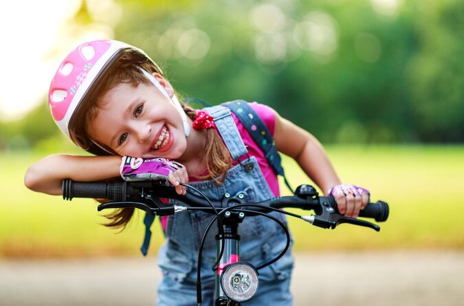 Lächelndes Mädchen mit Fahrradhelm sitzt auf einem Kinderfahrrad bei sonnigem Wetter.
