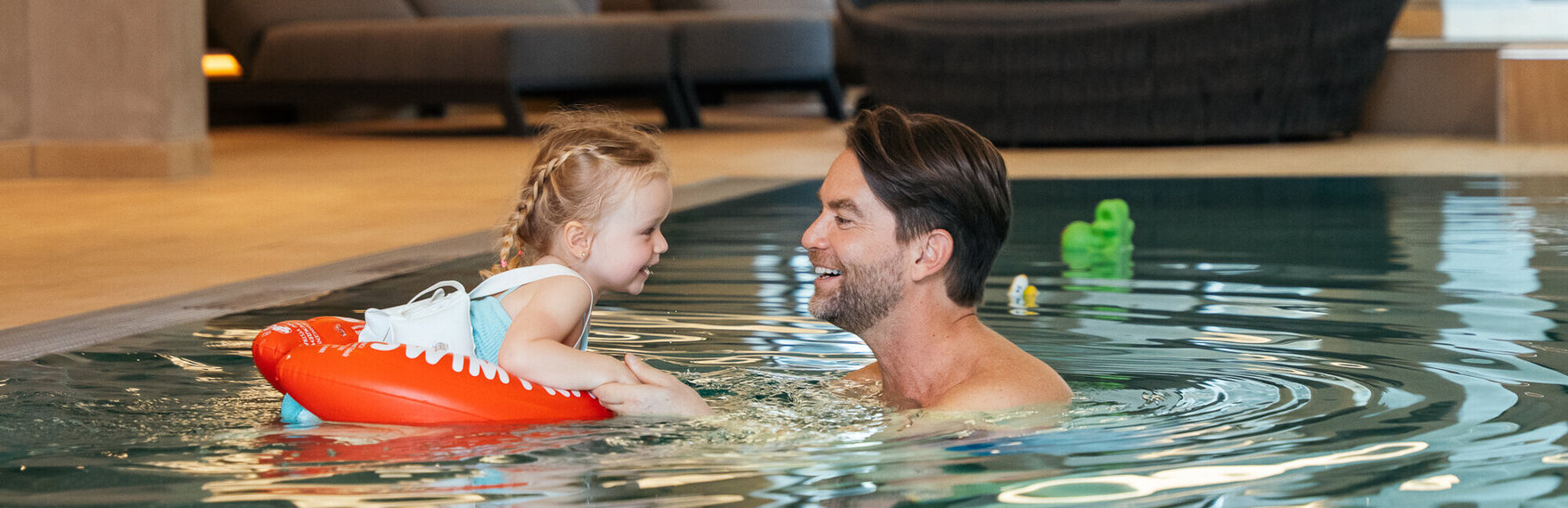 Vater und Tochter im Pool, die Tochter benutzt einen Schwimmreifen.